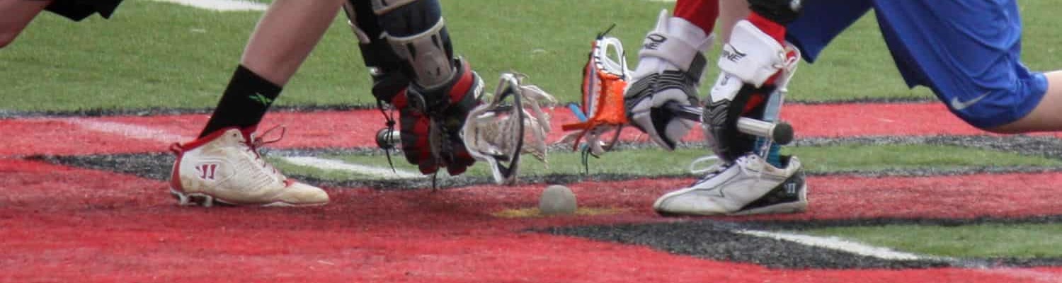 A rugby ball rests on synthetic turf with crisp white markings, as goalposts and tall trees stand in the blurred background of Albuquerque’s sports fields on a sunny day.
