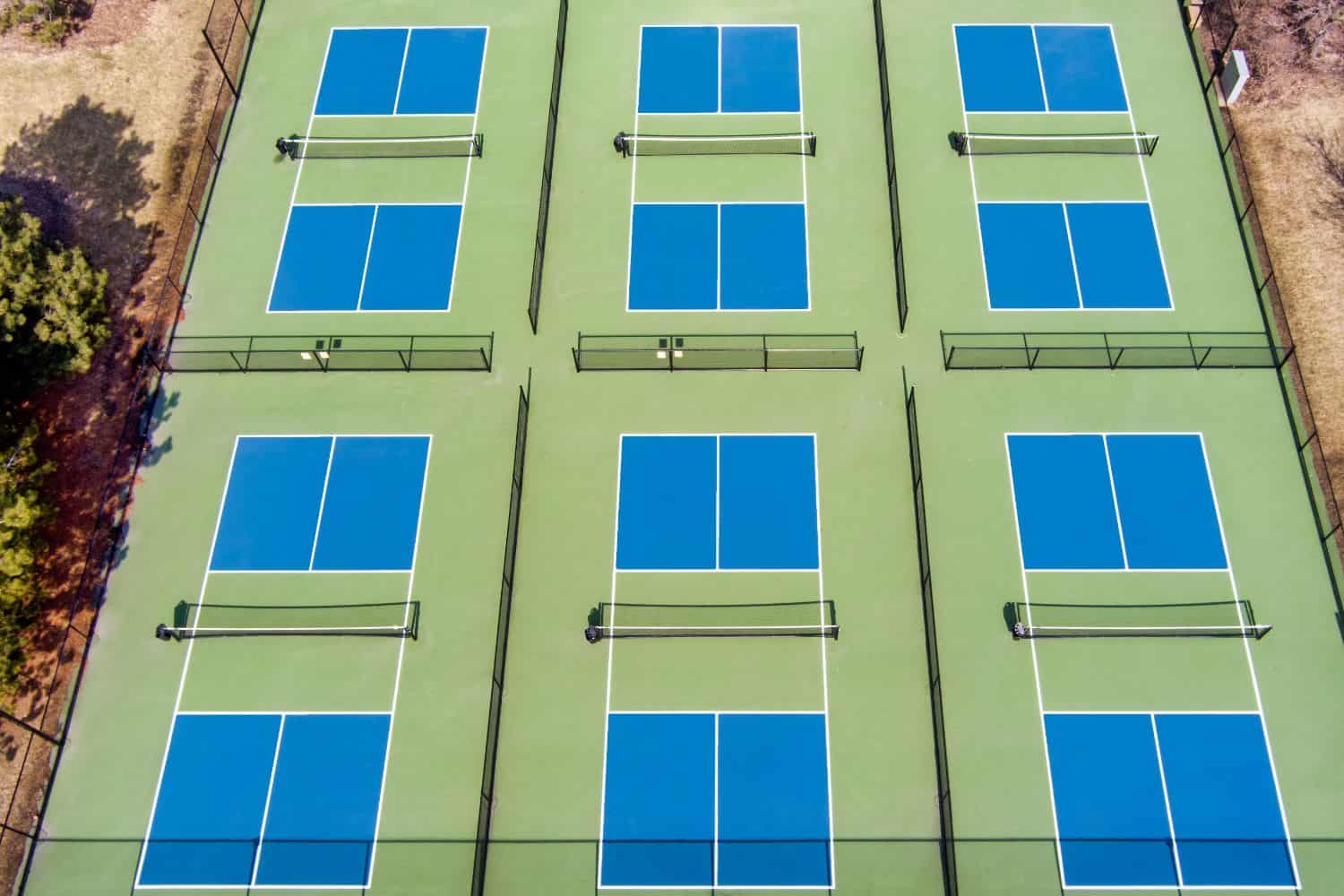 Four people playing pickleball on a sunny court with mountains in the background. Two men and two women are actively engaged, focused, and competitive.