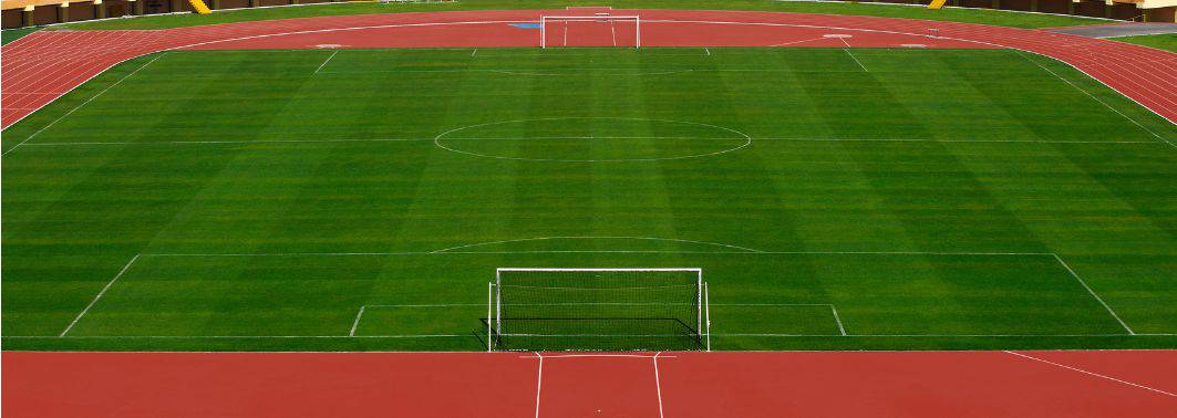 A view of an empty athletic field in Tucson AZ, featuring green synthetic grass, a red running track, and two white goalposts at either end. No athletes or spectators are present.