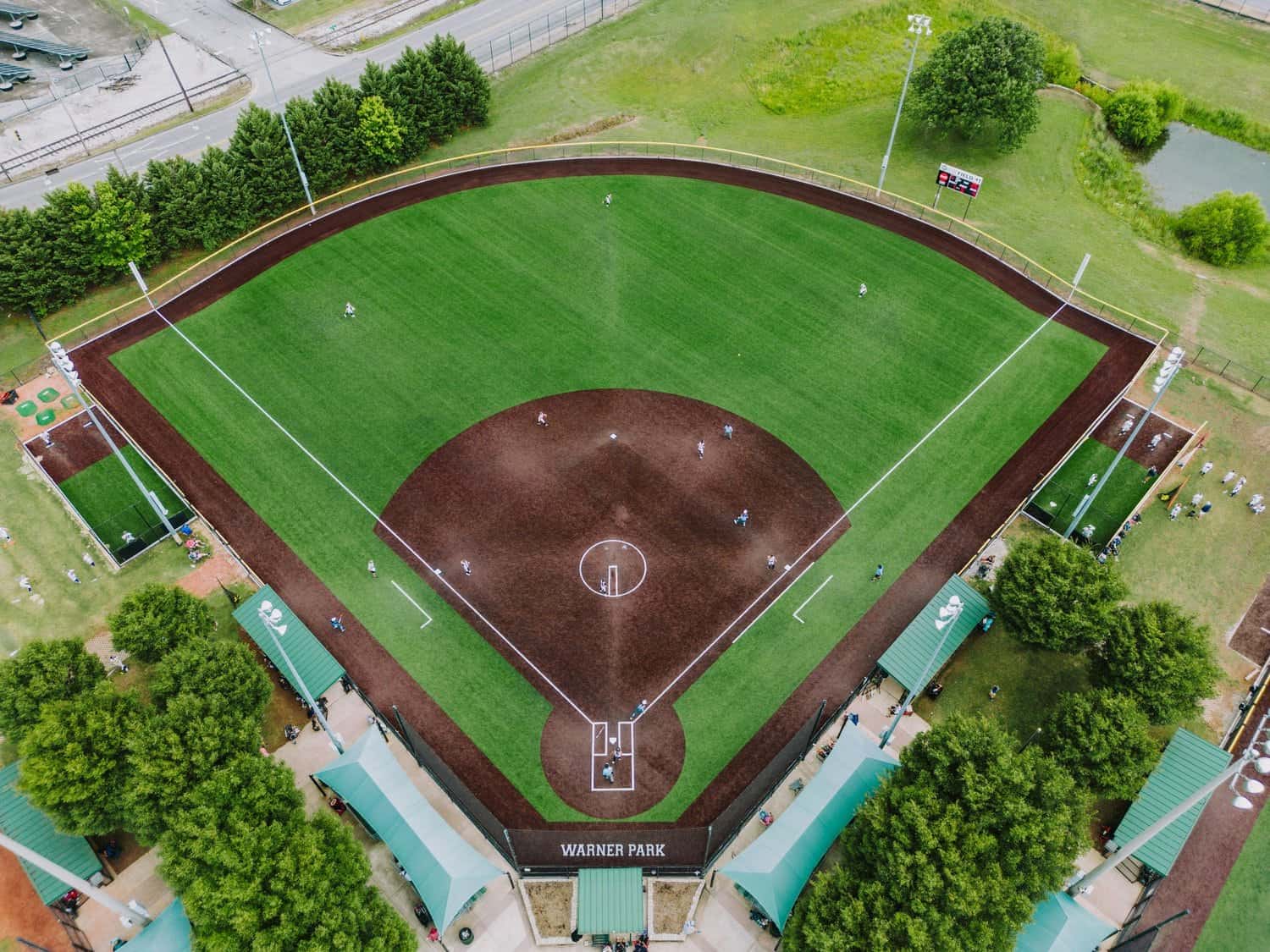 Two softball players in uniforms and helmets are on the sports field, one crossing home plate as the other approaches. Spectators watch from bleachers behind a chain-link fence, enjoying the benefits of quality artificial turf installation in Salt Lake City.