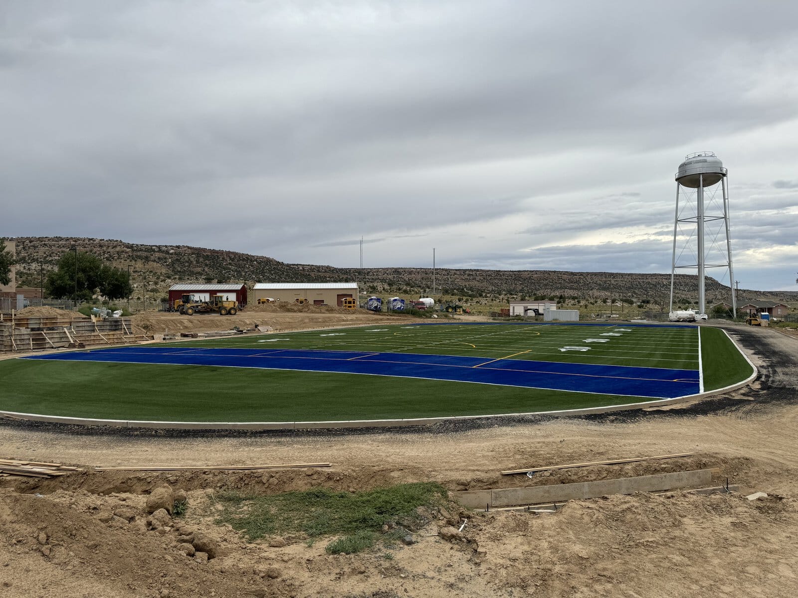 A young cricket player in protective gear prepares to hit a ball with a bat on sports turf. The ball is mid-air, and a set of stumps stands behind the player. Trees are blurred in the background.